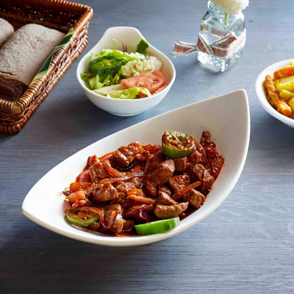Ethiopian Gored Gored, a dish of cubed beef in a spicy red sauce, served with injera and salad.