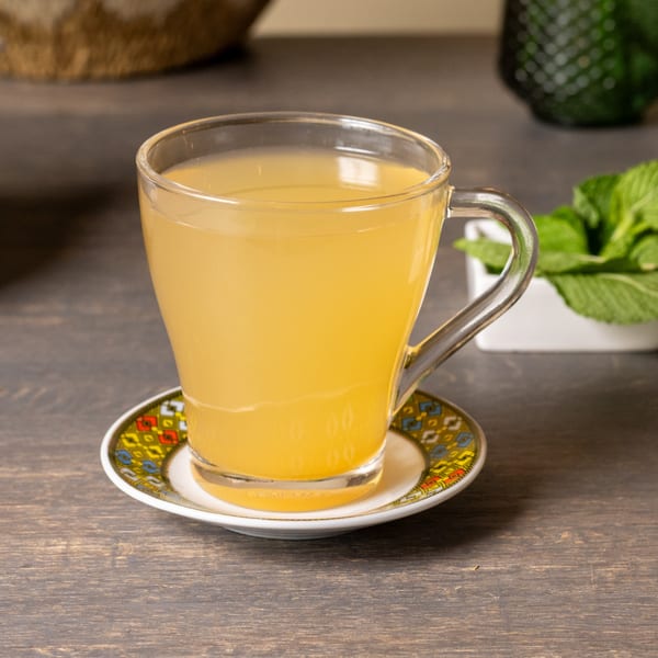 A clear glass mug of golden Ethiopian tea sits on a colorful saucer on a wooden table.