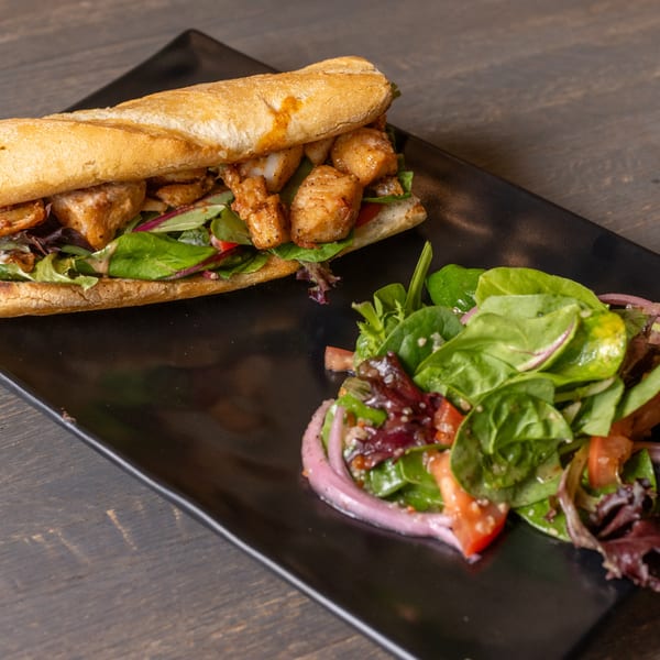 A chicken sandwich on a baguette with lettuce and red onion, served with a side salad.