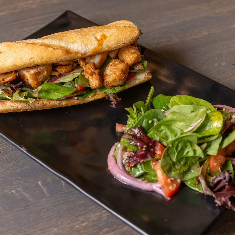 A chicken sandwich on a baguette with lettuce and red onion, served with a side salad.