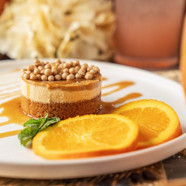 A dessert with two layers, topped with chickpeas and caramel, garnished with orange slices and mint.