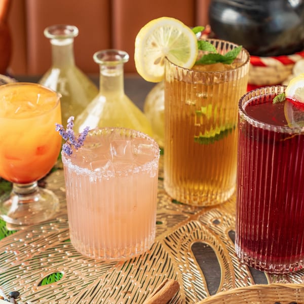 Four colorful Ethiopian drinks, including orange, pink, amber, and red, on a decorative gold tray.