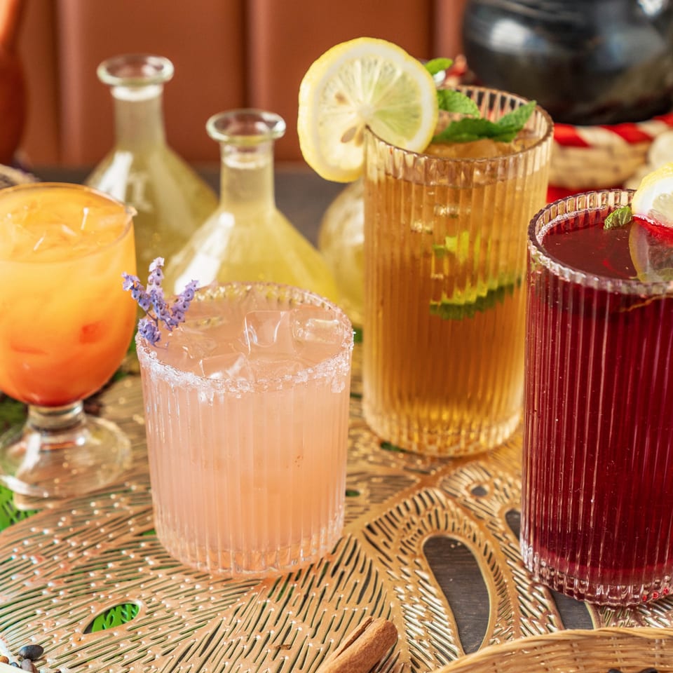 Four colorful Ethiopian drinks, including orange, pink, amber, and red, on a decorative gold tray.