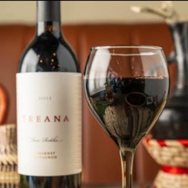 A bottle of Treana wine next to a glass of red wine, with traditional Ethiopian decor.
