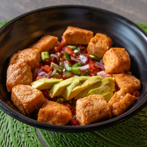 Spiced salmon cubes, avocado slices, and a colorful vegetable salsa in a black bowl.