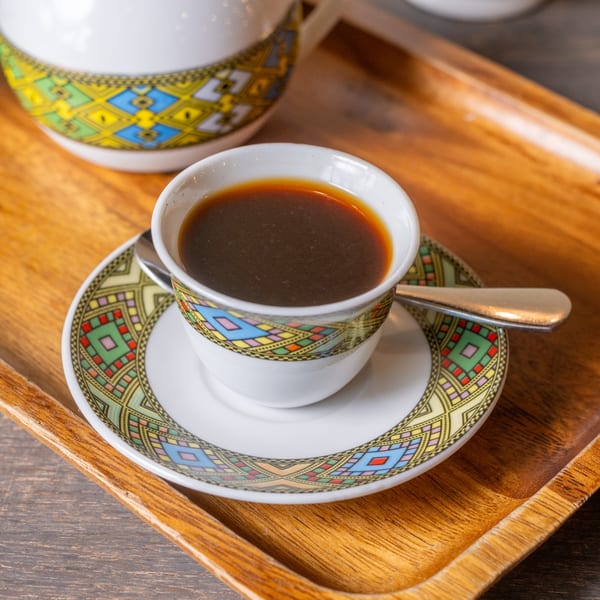 Ethiopian coffee in a traditional cup with colorful patterns, on a matching saucer and wooden tray.