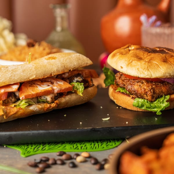 Two delicious sandwiches, one a sub and one a burger, on a dark serving board.