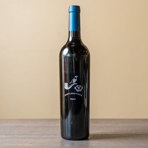A dark wine bottle with a blue foil top and a white bird-on-pipe logo stands on a wooden table.