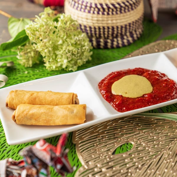 Two golden spring rolls and a dish of red sauce with a dollop of green sauce.