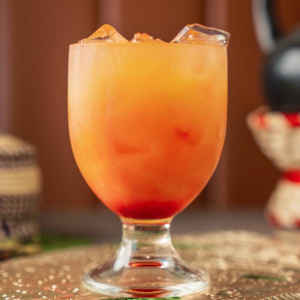 A vibrant orange and red layered drink with ice, served in a clear glass at Ethiopiques.