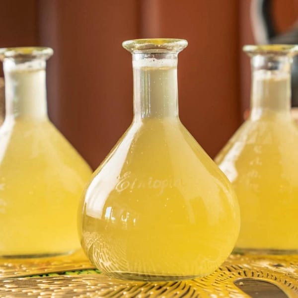 Three glass bottles filled with yellow Ethiopian honey wine, Tej, on a golden tray.