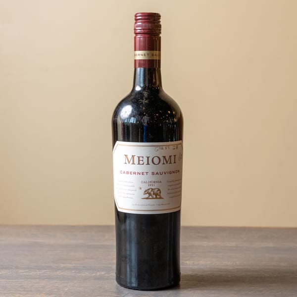 A bottle of Meiomi Cabernet Sauvignon wine with a red cap and white label on a wooden table.