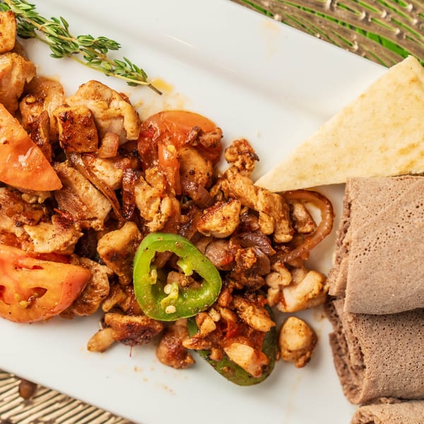 Ethiopian chicken tibs with tomatoes, peppers, and injera bread on a white plate.