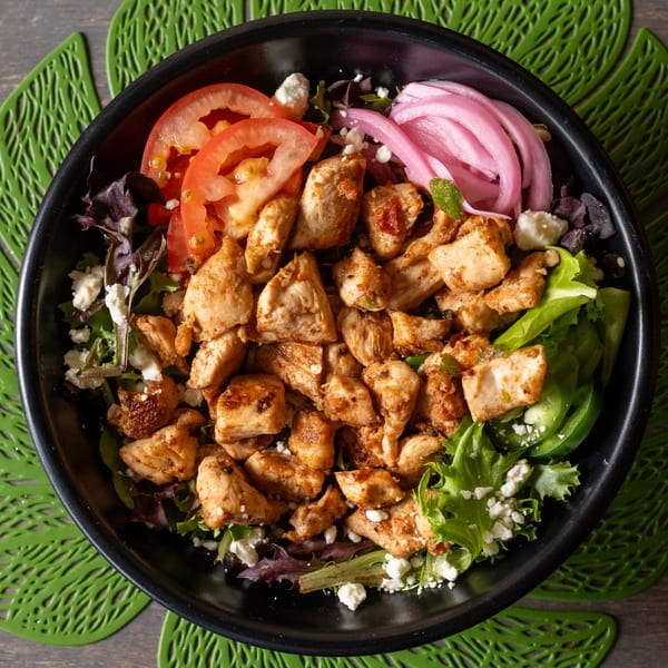 Top-down view of a chicken salad bowl with tomatoes, pickled onions, and feta cheese.
