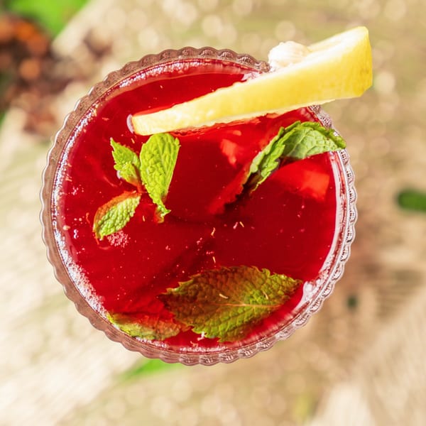 Top-down view of a vibrant red drink garnished with fresh mint leaves and a lemon slice.